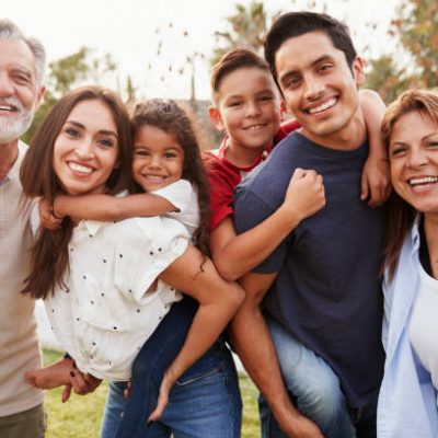 Three generation Hispanic family standing in the park, smiling to camera, selective focus
