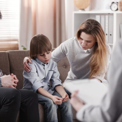 Mother hugging her autistic son, sitting next to a father during a family therapy